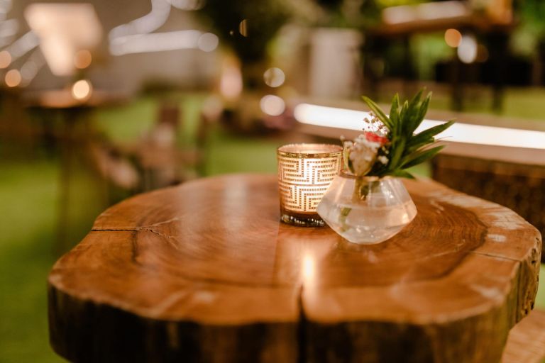 Romantic outdoor setting with a candlelit wooden table, adorned with a small flower arrangement. Perfect for event or wedding ambiance.