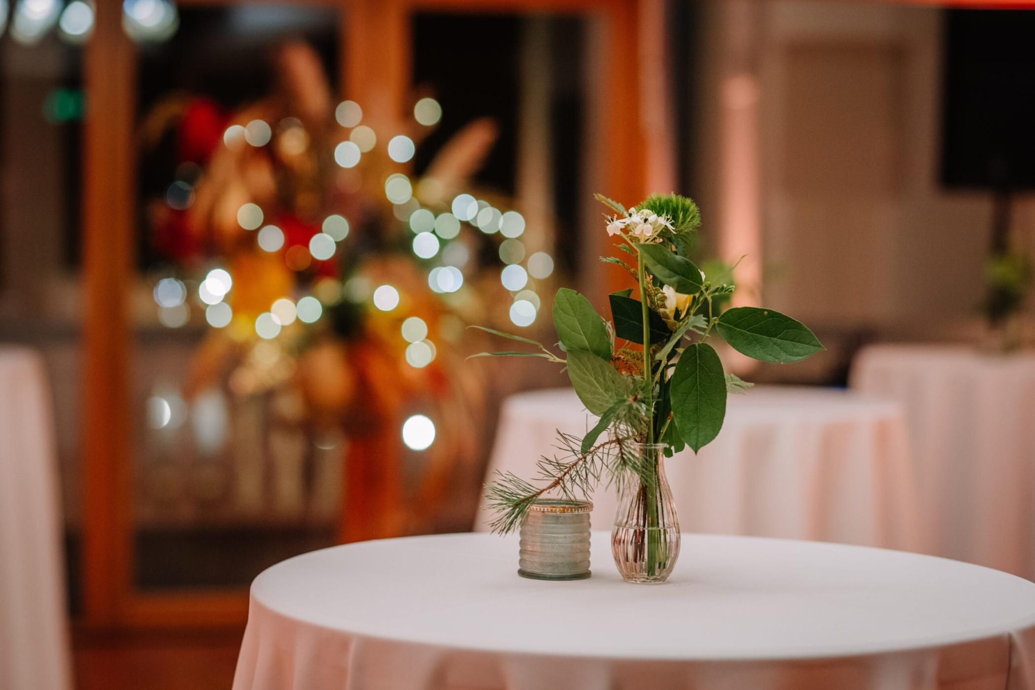A close-up of a small flower arrangement in a vase on a round table with soft bokeh lights in the background.