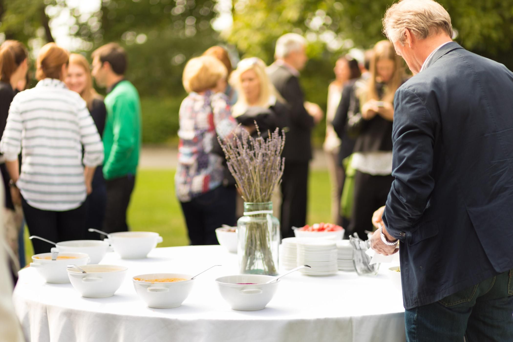 Banquet lunch break at conference meeting on hotel terrace. Assortment of food and beverage. Unrecognizable people discussing over food in background.